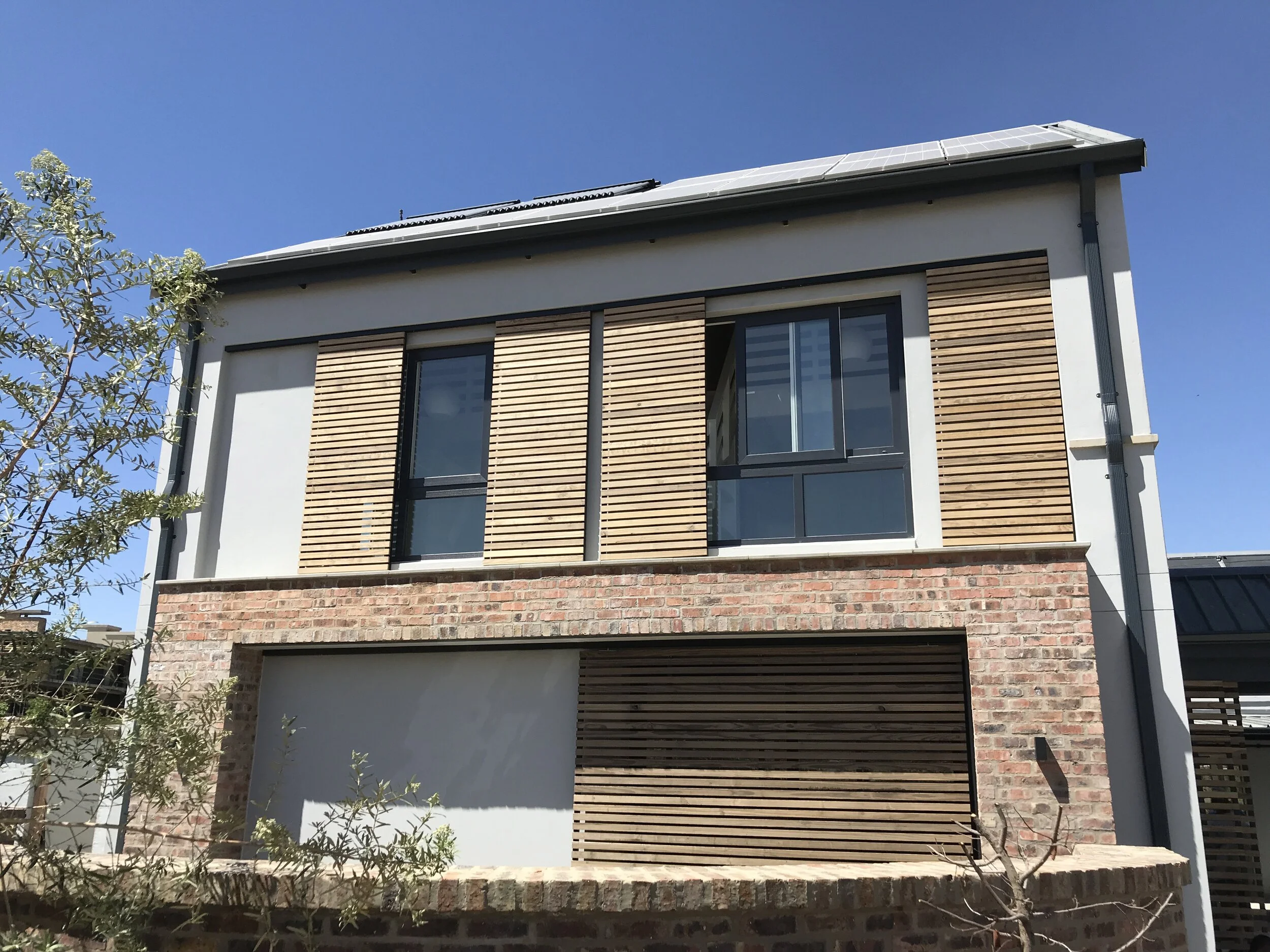 House facade with sliding timber slat screens over the windows and solar panels on the roof